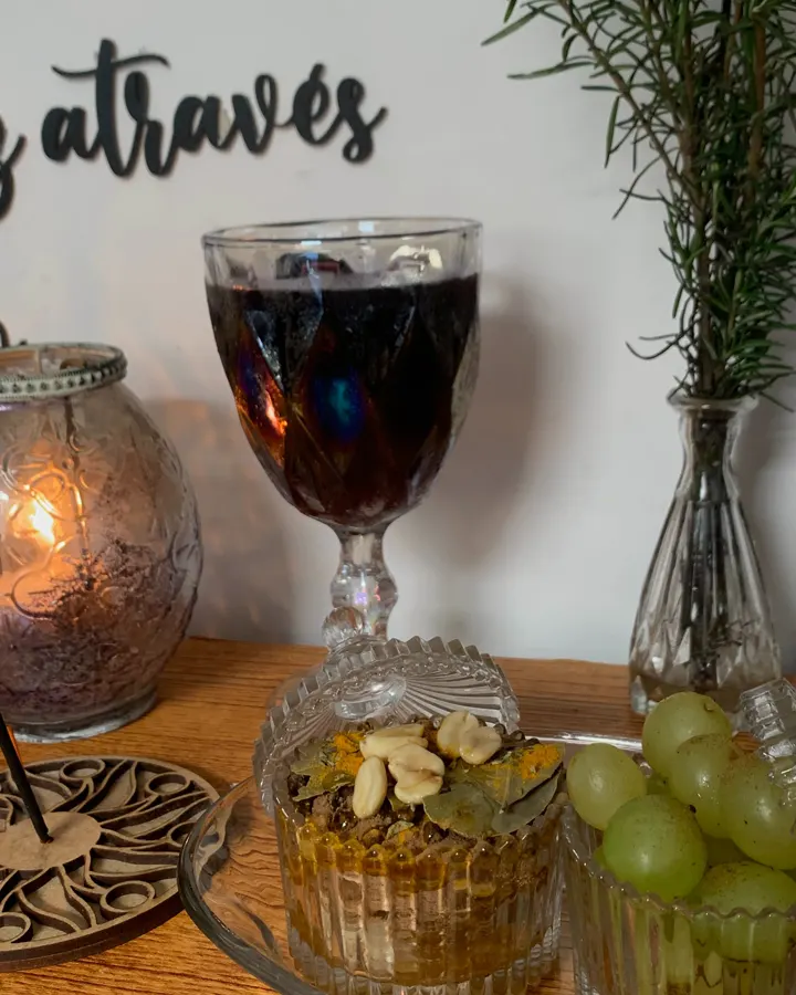 Mesa do espaço da Kakau com vela acesa, taça de vinho, uvas e alecrim, sob a frase buscando a luz através do oráculo